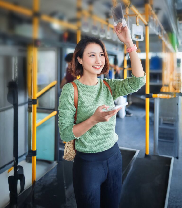 Young adorable joyful woman is standing on the bus using the phone and smiling